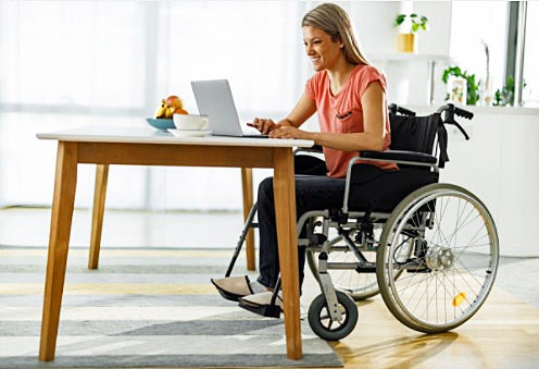 Delighted young woman at work on her computer laptop relaxing in a manual wheelchair at home.