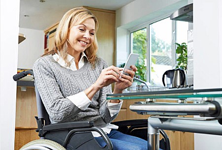 Woman relaxing in her manual wheelchair texting on a mobile phone at her home.